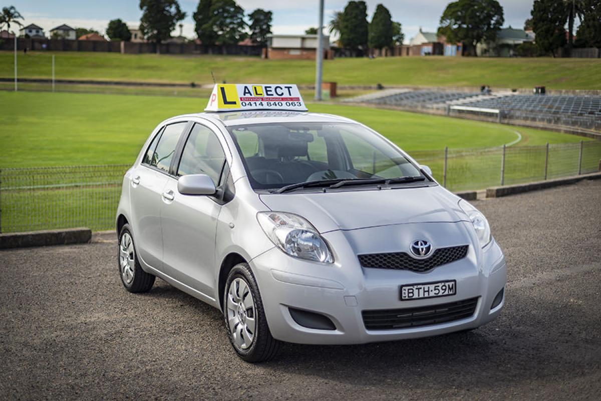 Silver learner driver Manual car with roof sign parked beside a sports field