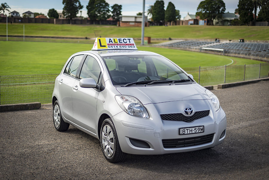 Silver learner driver Manual car with roof sign parked beside a sports field