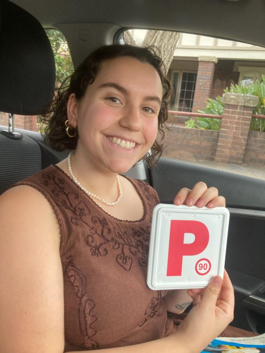 Smiling learner driver sitting in a car and holding a P plate sign
