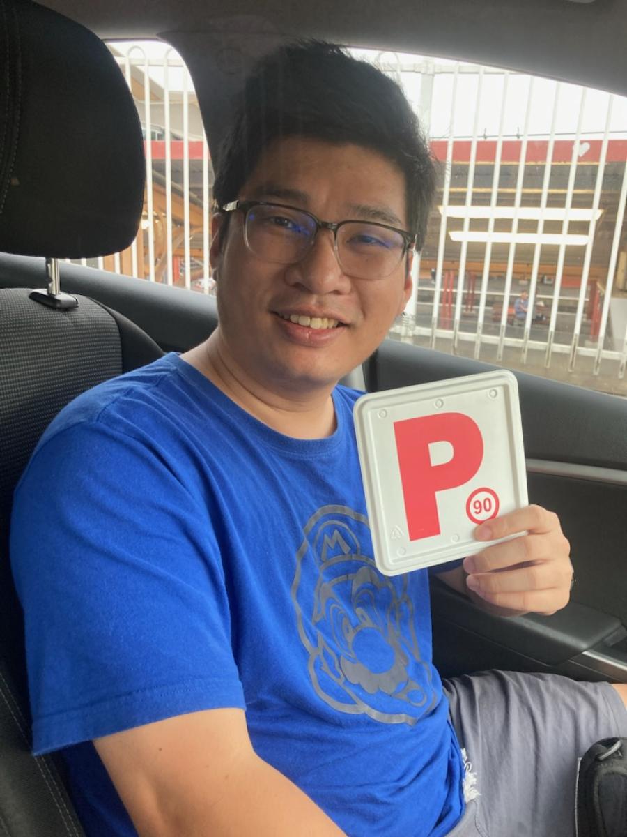 Smiling driver sitting in a car holding a red P plate after driving lessons