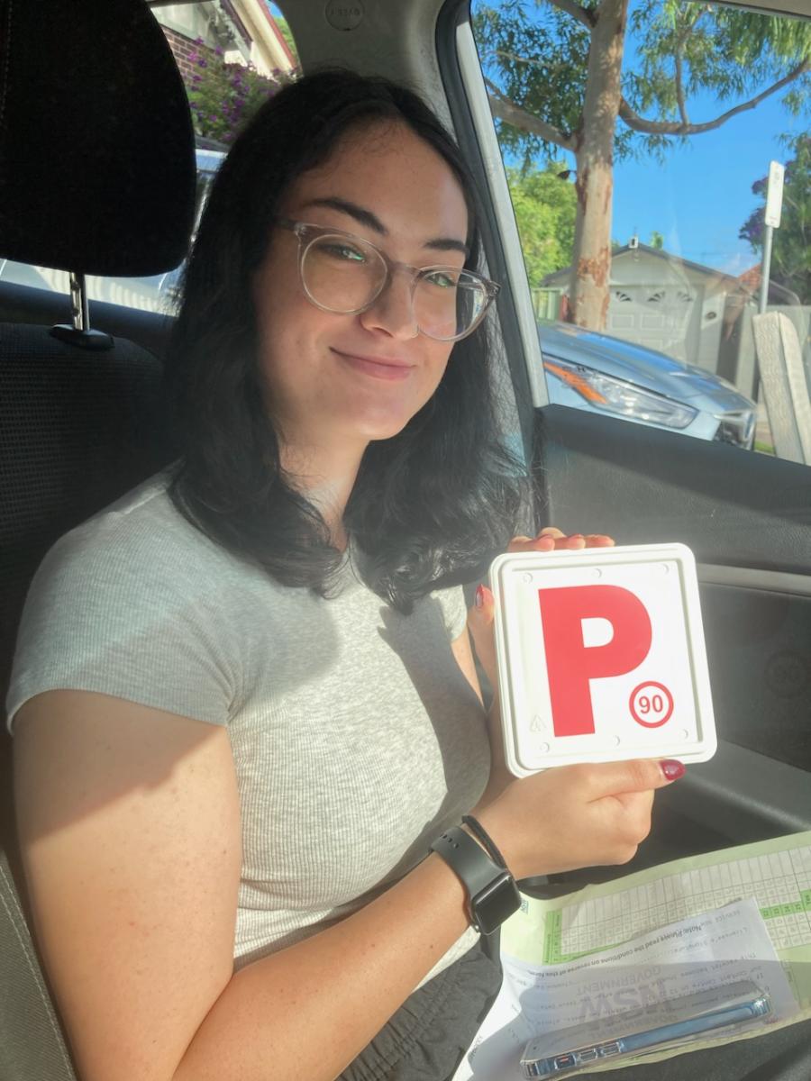 Learner driver sitting in a car holding a red P plate after a driving lesson