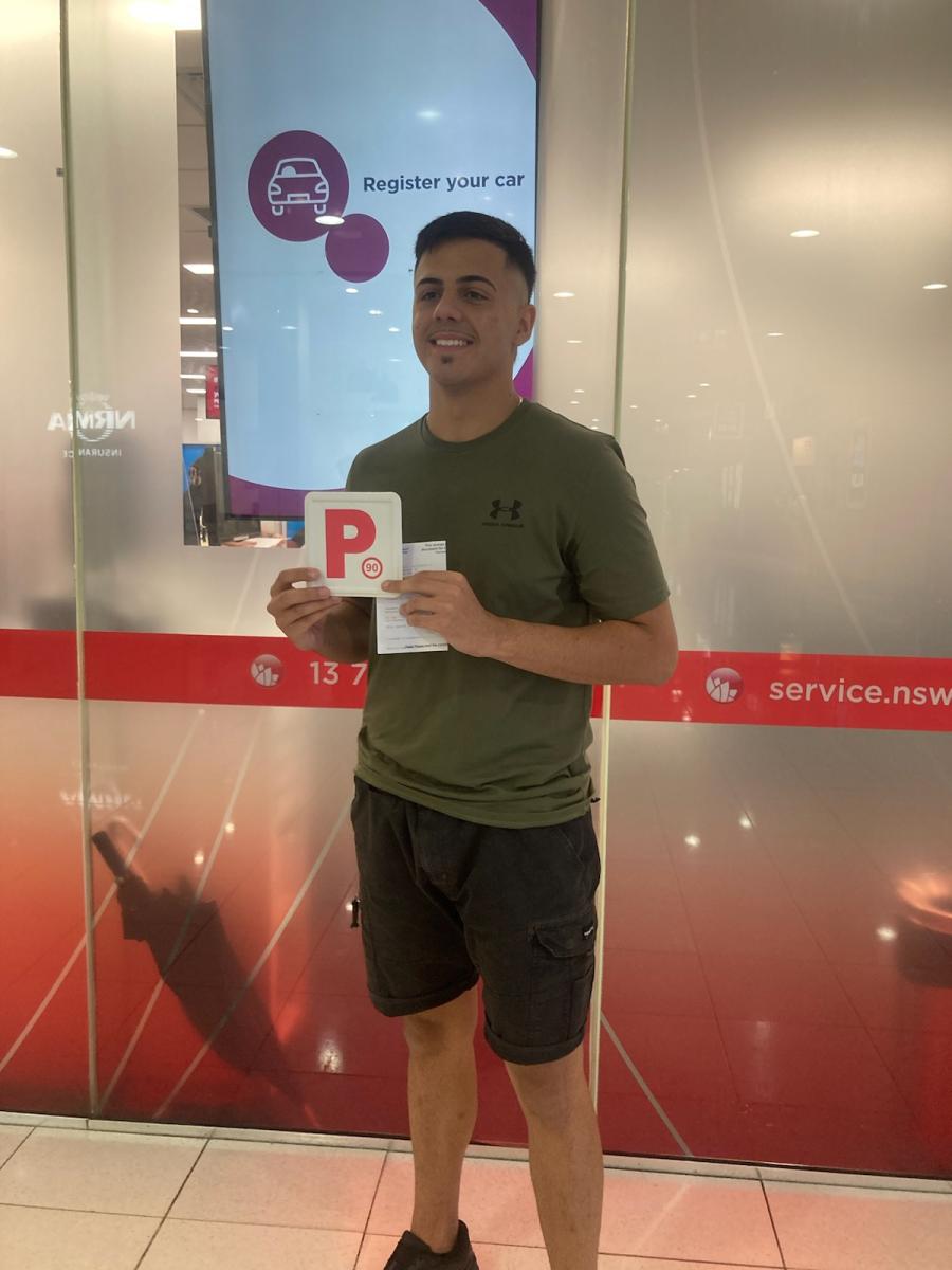 Smiling learner driver holding a red P plate after passing a driving test