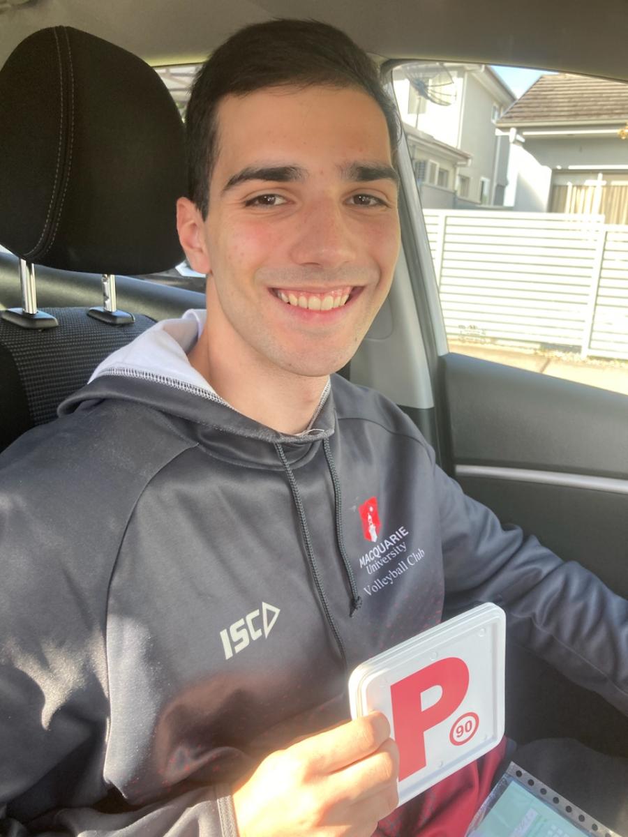 Smiling learner driver sitting in a car holding a red P plate after driving lessons