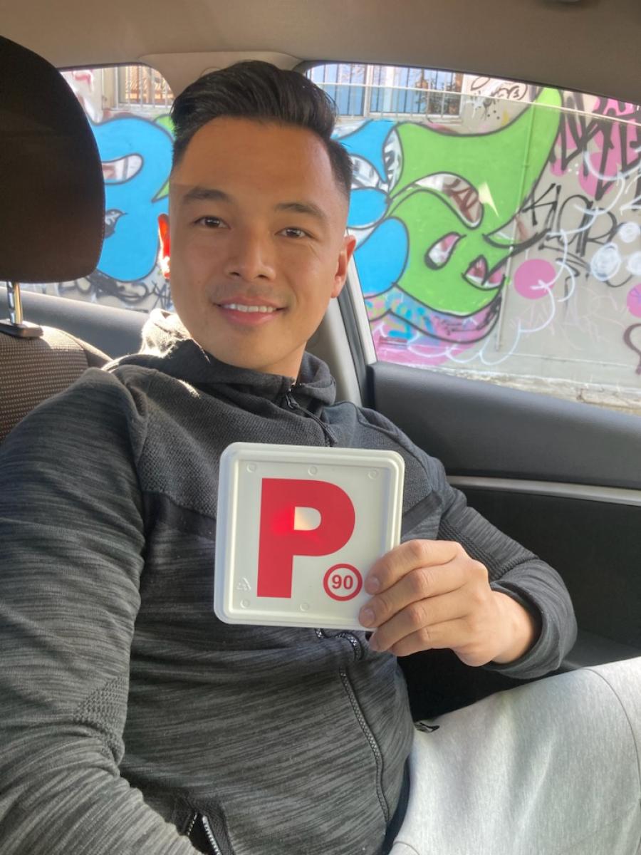 Smiling driver sitting in a car and holding a red P plate after passing a driving test