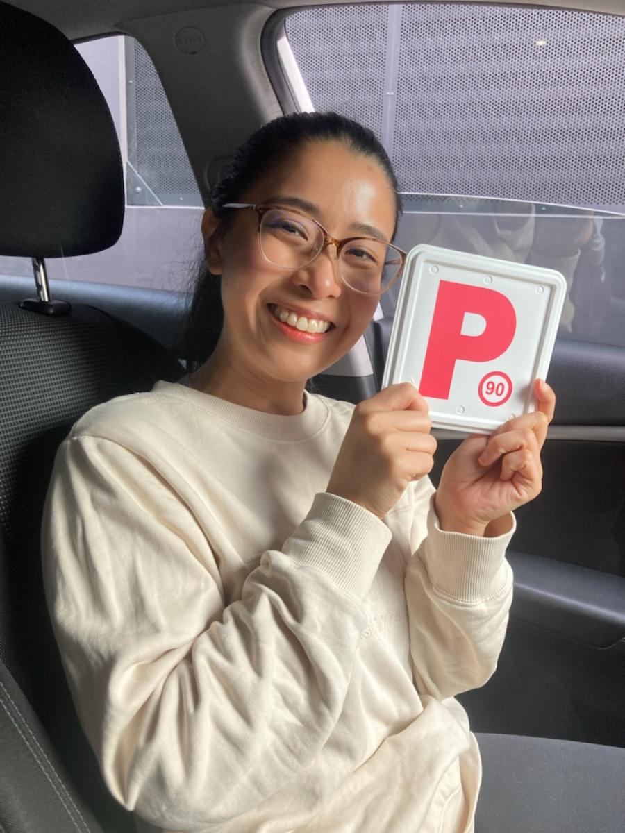 Smiling new driver sitting in a car and holding a red P plate