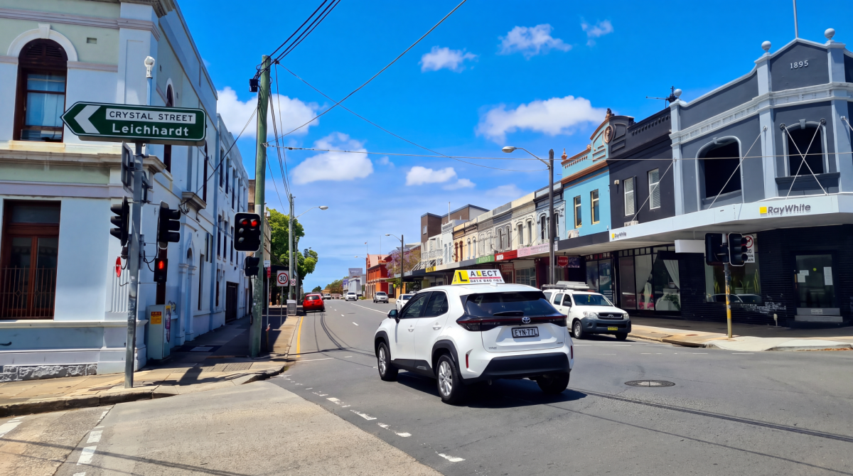 White car driving through a town centre street with shops and clear road markings
