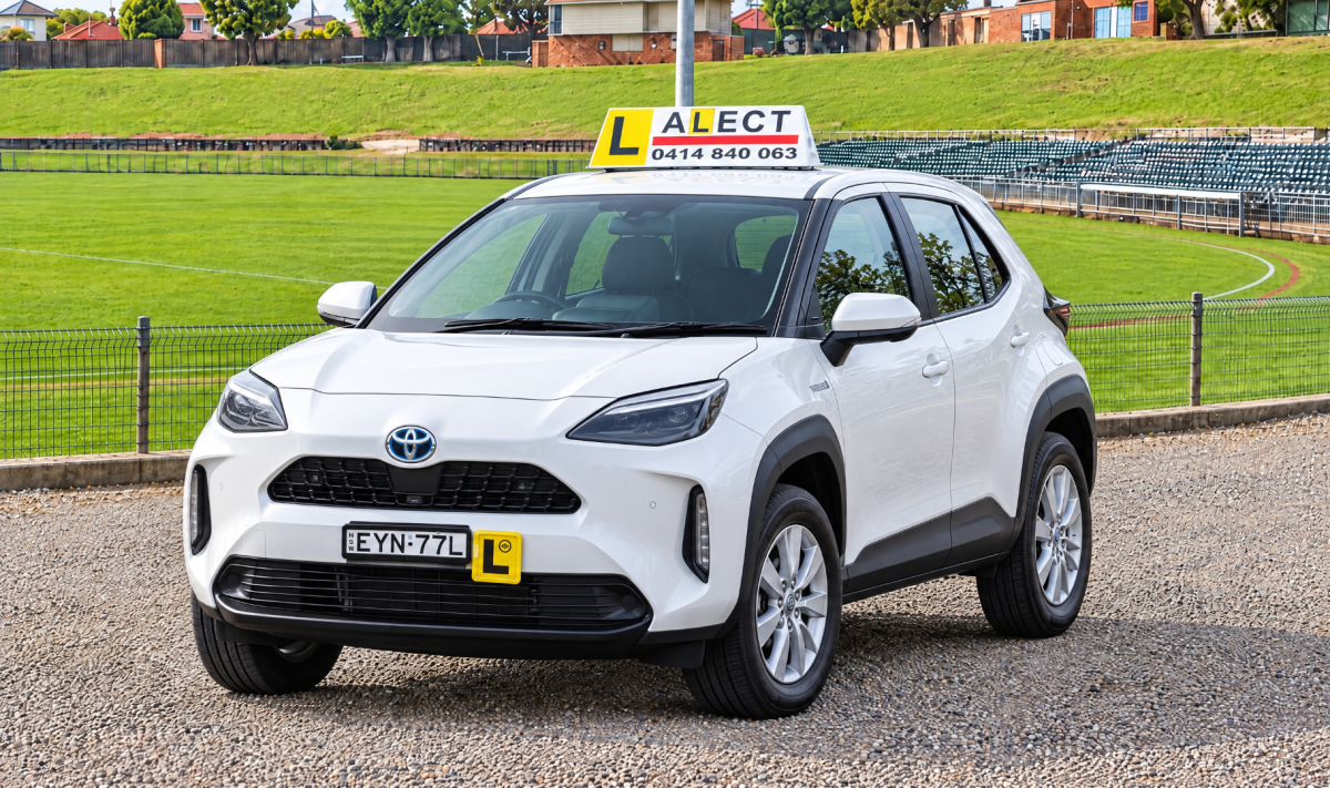 White learner driver car with roof sign parked beside green open space