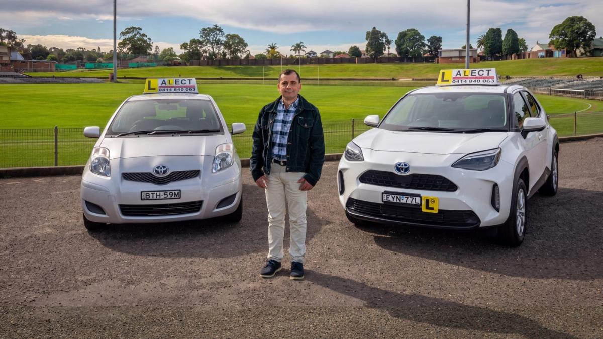 David Abreu standing between two learner driver cars in an outdoor car park