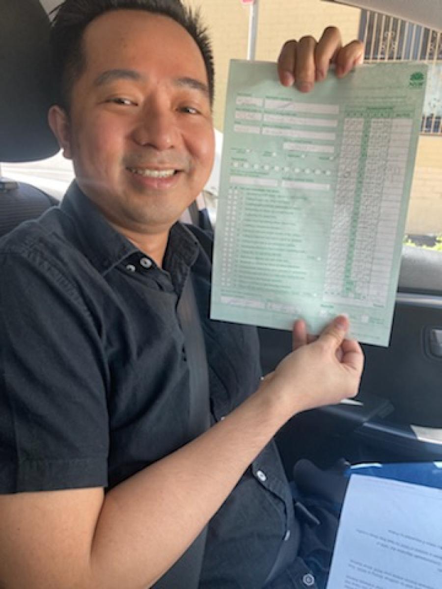 Smiling learner driver holding a driving test pass certificate inside a car