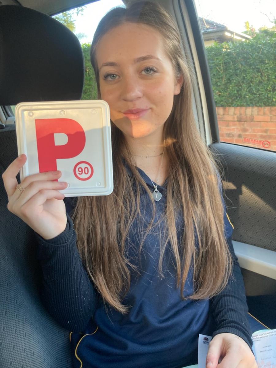 Learner driver smiling in a car while holding a red P plate