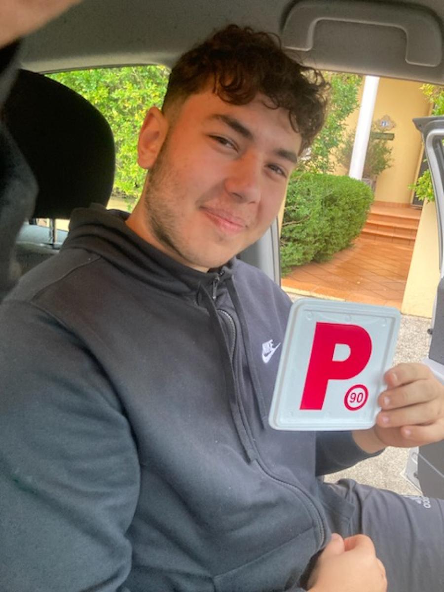 Smiling learner driver sitting in a car holding a pass certificate