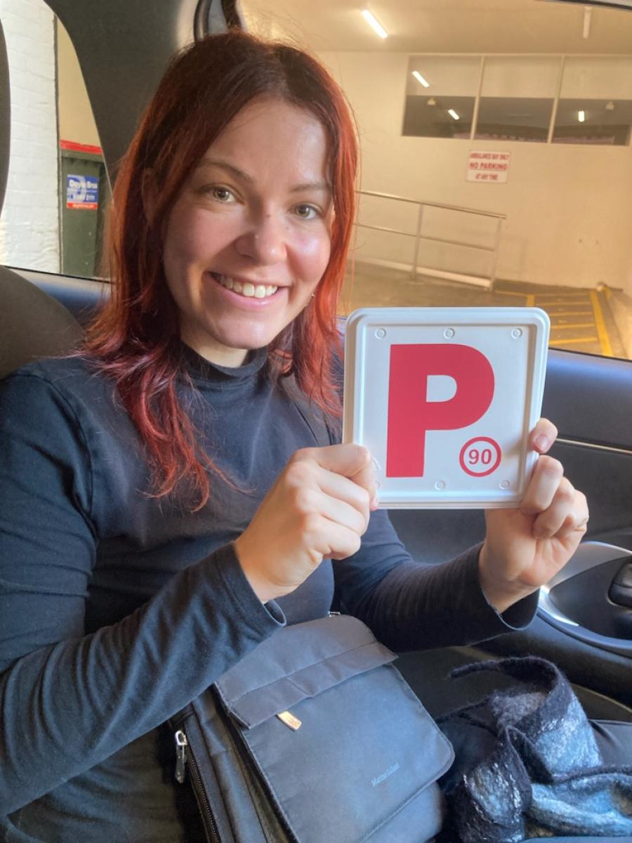 Smiling learner driver sitting in a car and holding a red P plate